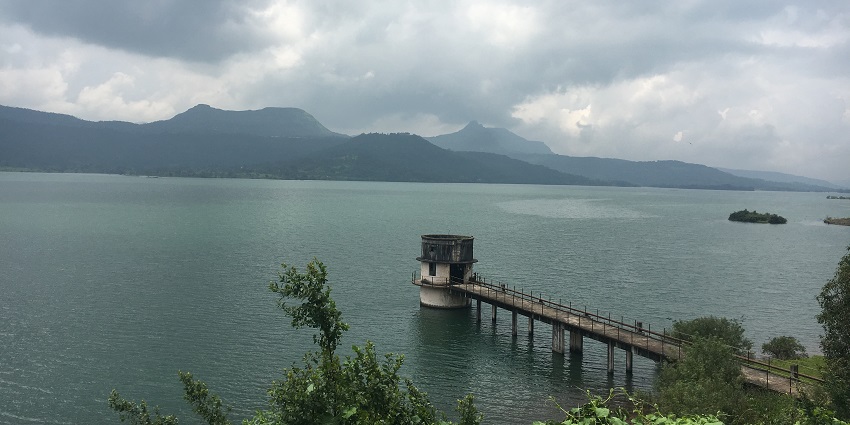 A picture of Pavana Lake with rain clouds above it and surrounded by misty hills