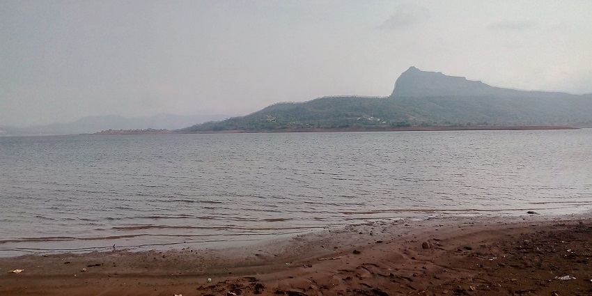 A majestic view of Pawna Lake in Maharashtra, India, with blue waters surrounded by lush green.
