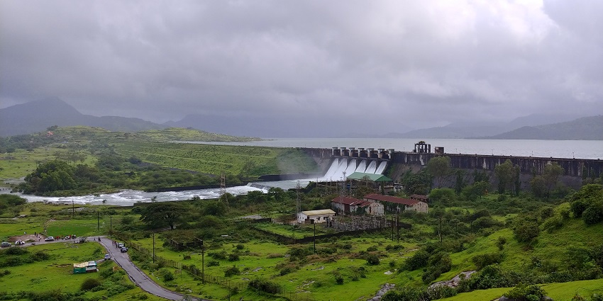 Dam surrounded by greenery and tourist cars on a road in the Pawna Lake Reservoir