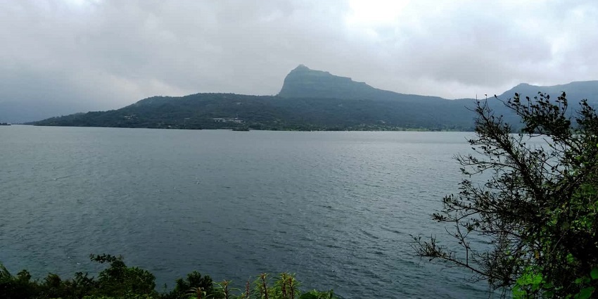 A serene view of the Pawna Lake alongside which there is greenery and mountains