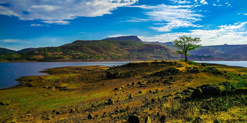 The picture of the shore of clear blue Pawna Lake surrounded by high-peak mountains.