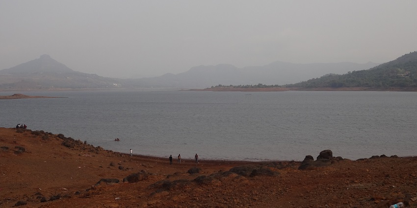 Camping tents set up along the shores of Pawna Lake with calm water and hills around