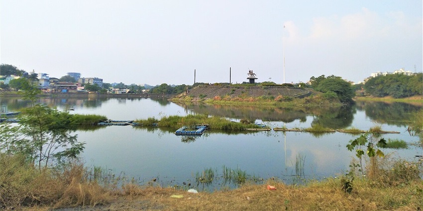 Picturesque view of the Pawna Lake, surrounded by lush greenery on a sunny day.