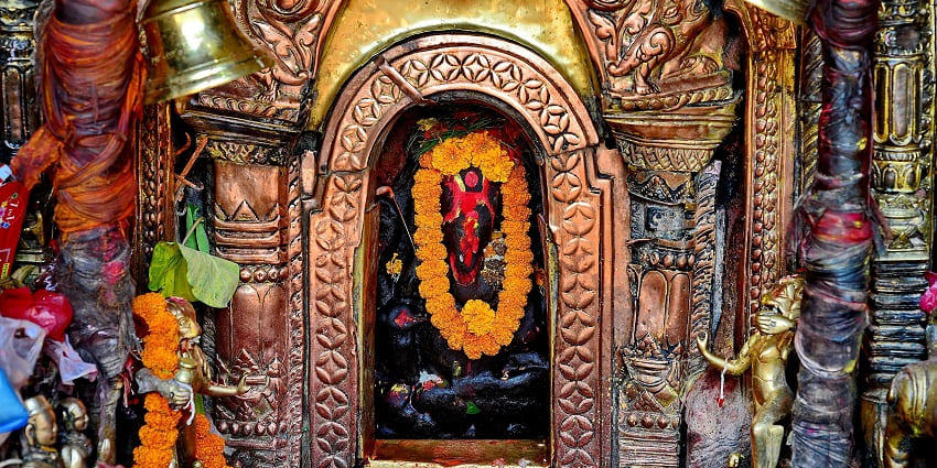 A mesmerizing black stone idol of lord Ganesha, adorned with gardland and vermillion