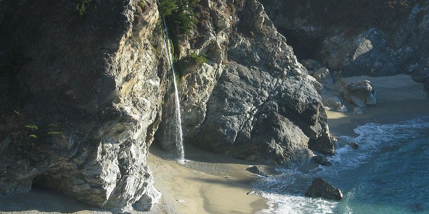 Waterfall cascading from a cliff onto a beach, flowing into the ocean of an island.