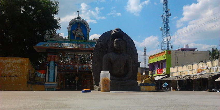A statue of Buddha in Perumathur, set against a backdrop of trees and foliage.