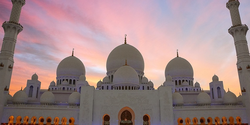 A picture of a white mosque taken from the front with sky visible in the background