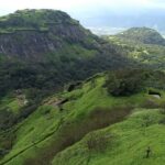 Side view of Rajmachi Fort exhibiting lush greenery, cliffs, and a clear blue sky