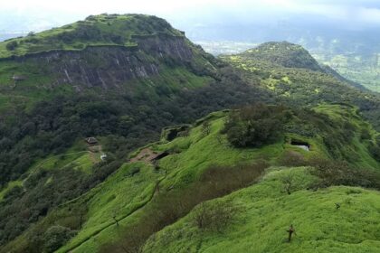 Side view of Rajmachi Fort exhibiting lush greenery, cliffs, and a clear blue sky