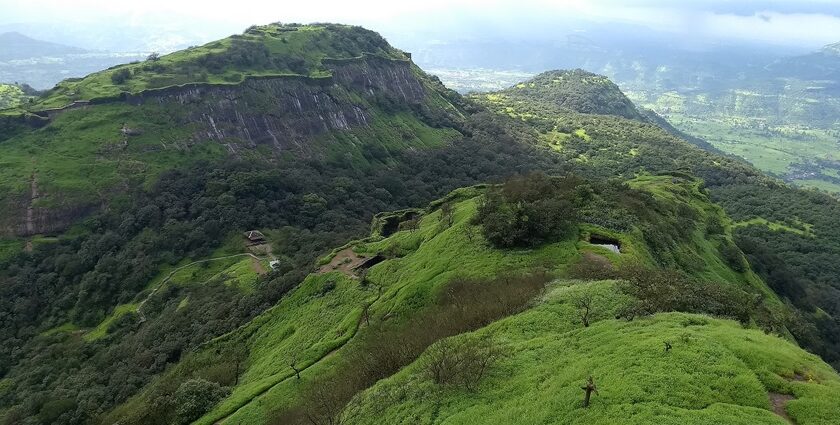 Side view of Rajmachi Fort exhibiting lush greenery, cliffs, and a clear blue sky