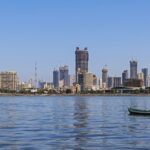 A picture of Mumbai’s skyline, featuring buildings, boats, sea, and lush greenery.