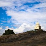 A glimpse of a temple nestled on a hill and surrounded by misty clouds in Karnataka.