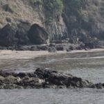 A glimpse of rhythmic waters hitting the shorelines of a beach decked with giant rocks.