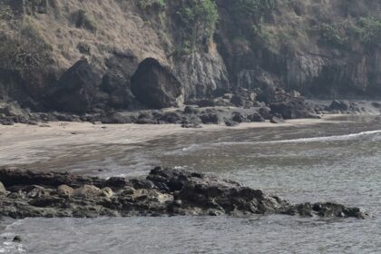 A glimpse of rhythmic waters hitting the shorelines of a beach decked with giant rocks.