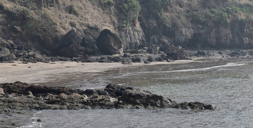 A glimpse of rhythmic waters hitting the shorelines of a beach decked with giant rocks.