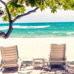 Chaise lounges under a tree on the beautiful tropical beach with white sand in Bali.