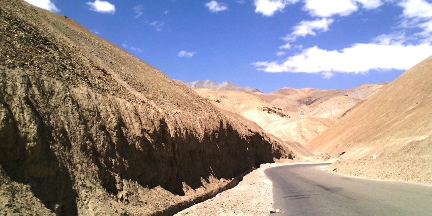 Image of a lonely dusty road to Ladakh, under the clear blue sky surrounded by mountains
