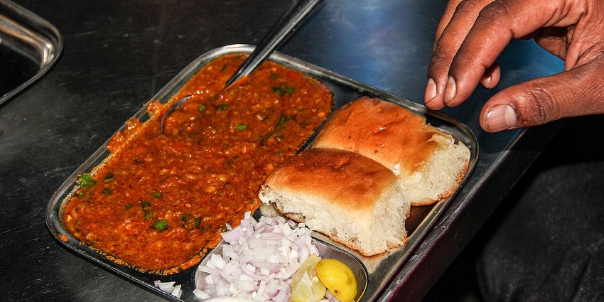 Bhaji served with two pavs with chopped onions and lemon on the side on a silver platter