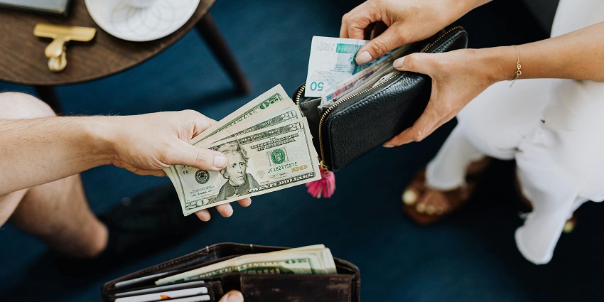 Two people exchanging various banknotes of different currencies on a coffee table.