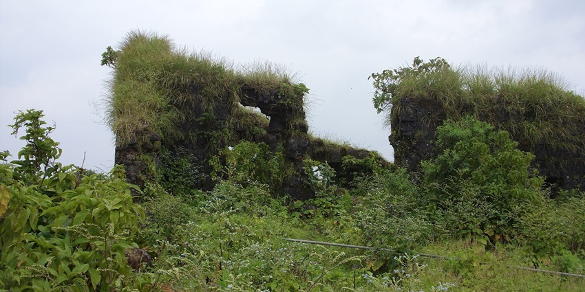 Ruined stone walls of Purandar Fort on a steep hill, surrounded by lush greenery.