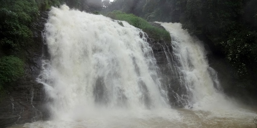Waterfall flowing down rocks, surrounded by trees and foliage.