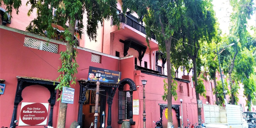 A picture of Raja Dinkar Kelkar Museum painted in red with trees on the border.