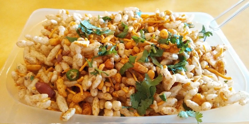 Bhelpuri, puffed rice mixed with sev, onions and tomatoes with chutney served with a spoon