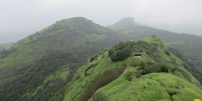 An immense stone water tank sits among greenery at Rajmachi Fort
