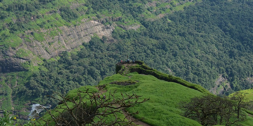 Rajmachi Fort from above with people sitting near the edge surrounded by other hills.