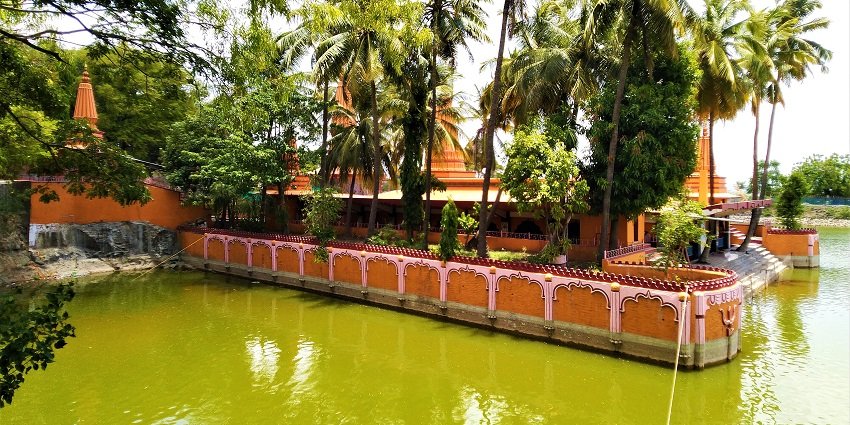A picture of a temple at the bank of a lake, with pine trees also visible in the background