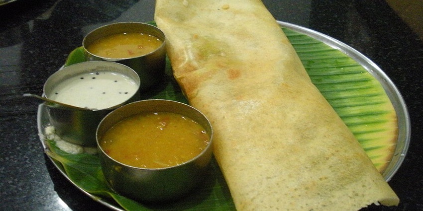 A Crispy Dosa with sambar and coconut or tomato chutney is placed on a banana leaf, one of the best food in Bandra.