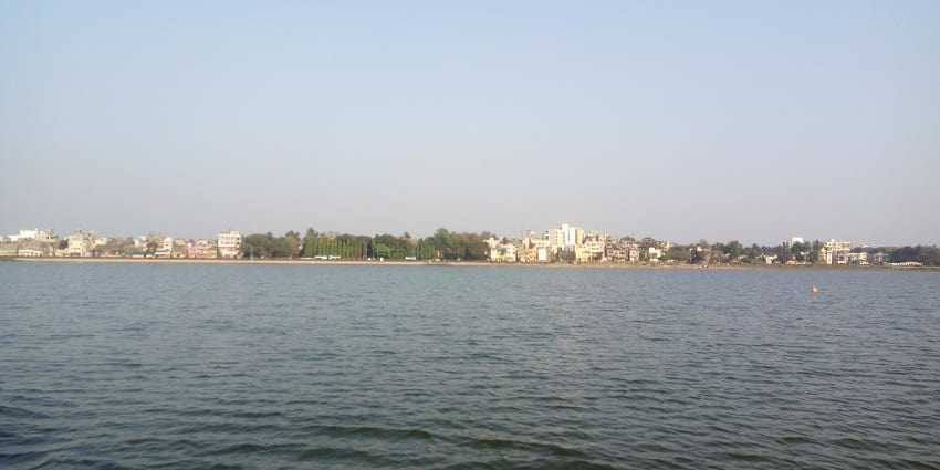Serene lake surrounded by lush greenery, reflecting the cloudy sky on calm waters in Kolhapur