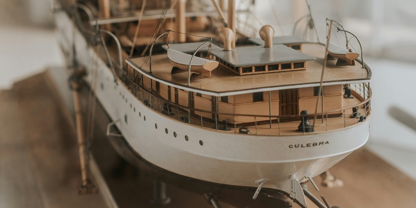 A toy boat displayed inside a marine museum, placed on a wooden surface with details.