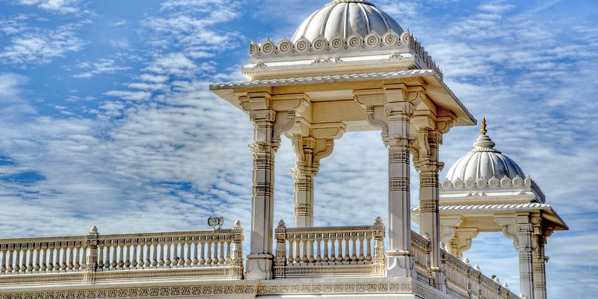 A stunning Hindu temple with elaborate carvings, surrounded by greenery under blue sky.