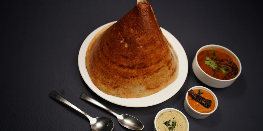 Dosa in a cone-shaped served on a plate accompanied by Sambhar and tomato and coconut dips