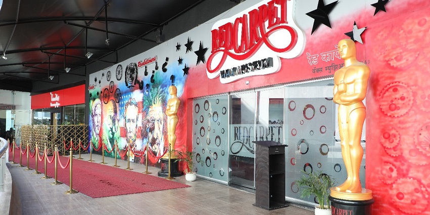 Red Carpet Wax Museum entrance with Oscar-like statues, red rope barriers, and mural art.