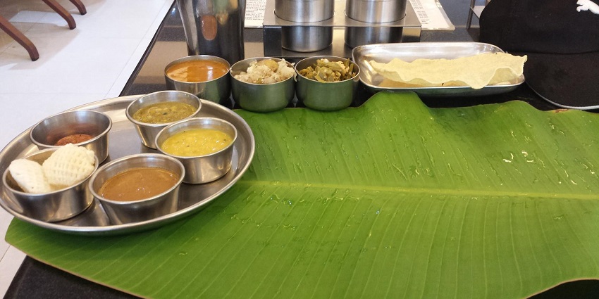 South Indian thali consisting of rasam, chutneys and papad, with a cleaned banana leaf.