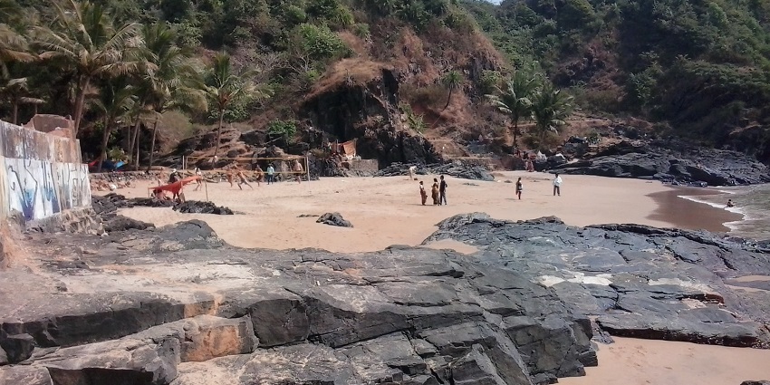 A beach view in Gokarna, India, with a golden shoreline and lush green hills in the background.