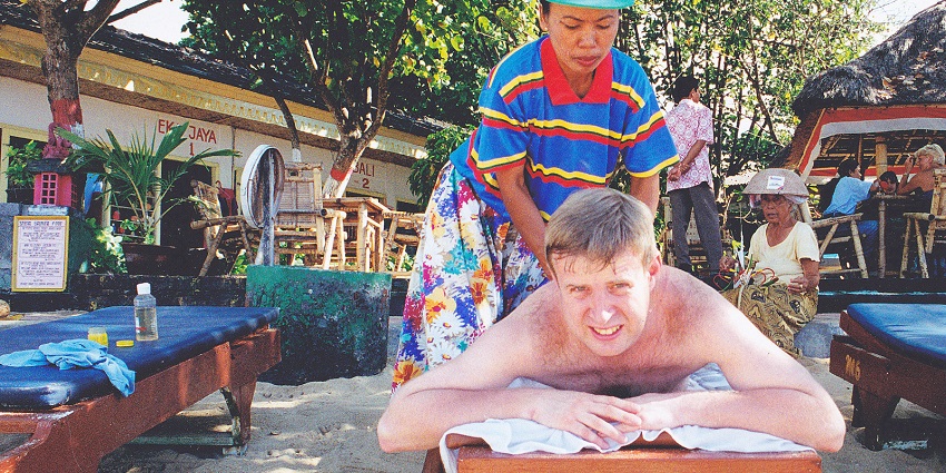 A woman giving a Balinese Massage to a tourist near a beach.