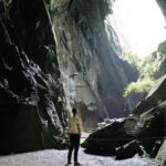 A breathtaking inside view of a lush green cave with a man standing inside in the day.