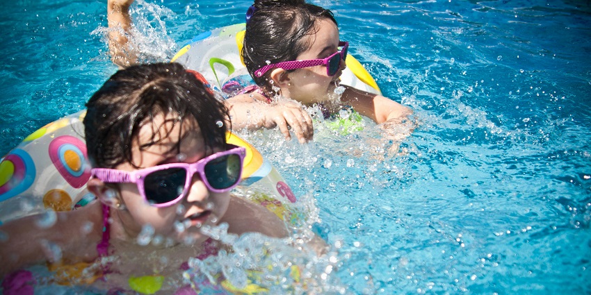 Two girls swimming in a pool during the day, with clear water and blue sky in the background.