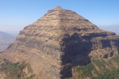 A panoramic view of Salher Fort against a blue sky with lush greenery surrounding it