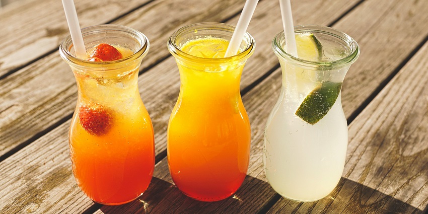 A variety of juices served in glasses accompanied by straw topped with fresh fruits