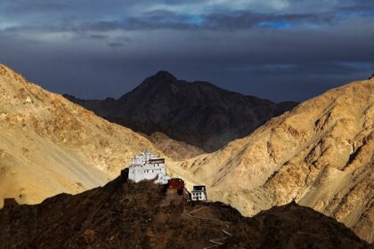 A picture of a monastery perched on top of a hill in Leh with multiple mountains visible in the background