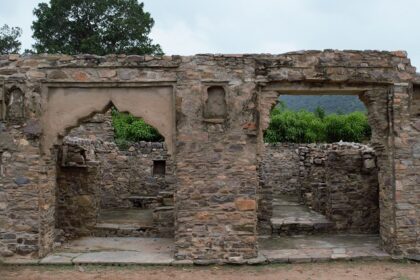 Ruins of Bhangarh Fort with remnants of stone structures and green barren hills.