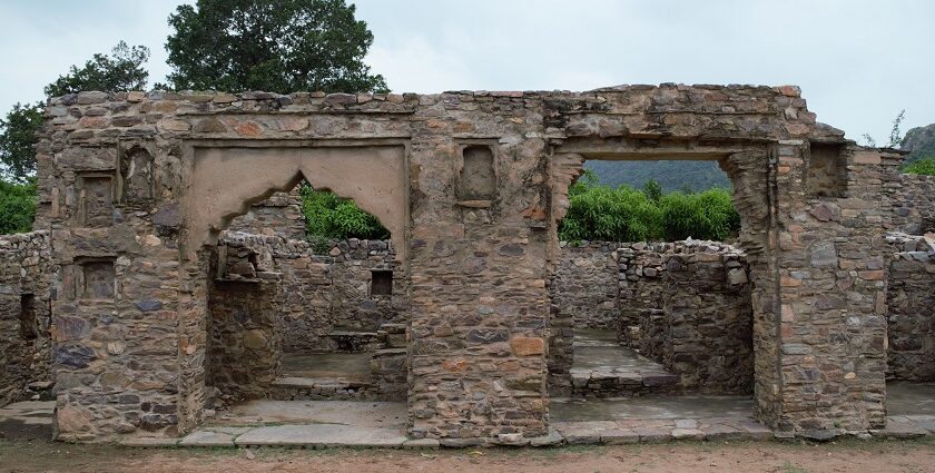 Ruins of Bhangarh Fort with remnants of stone structures and green barren hills.