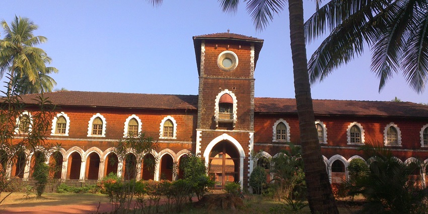 Red brick building with arched windows and clock tower, surrounded by palm trees.