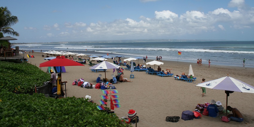 People relaxing at the beach with greenery and umbrellas near the shoreline