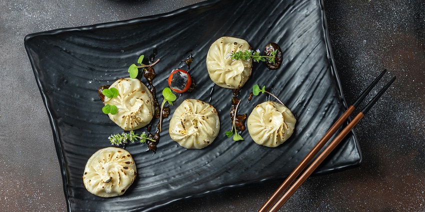Momos served on a black plate garnished with a variety of herbs and sauce drizzled on a plate