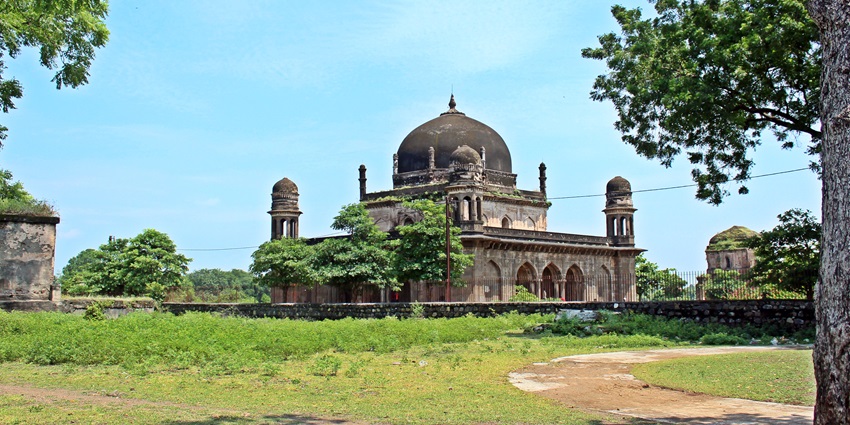 A picture of a historical tomb with black exteriors, surrounded by lush green gardens